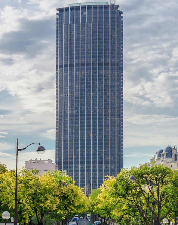 Montparnasse Tower in Paris with tree-lined street in foreground.