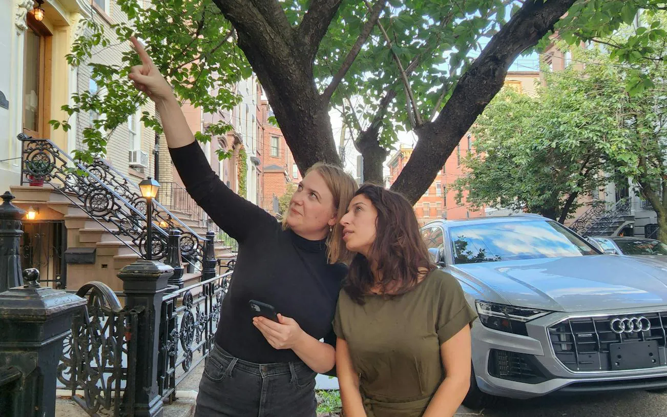 Two people exploring a tree-lined street in New York, part of a self-guided city exploration game.