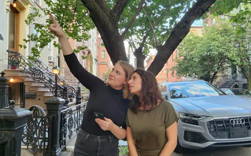 Two people exploring a tree-lined street in New York, part of a self-guided city exploration game.