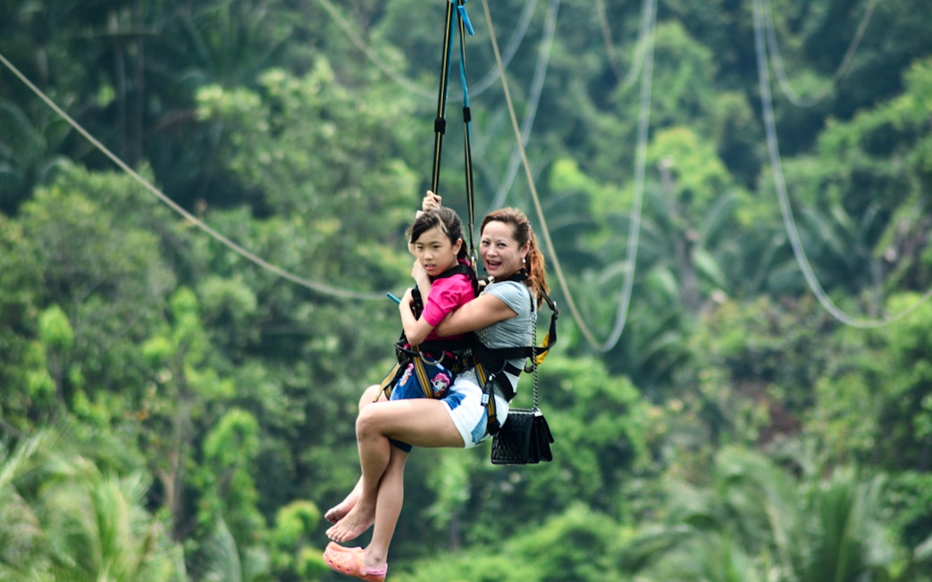 Two people zip-lining through lush greenery in Singapore.