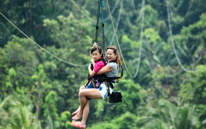 Two people zip-lining through lush greenery in Singapore.
