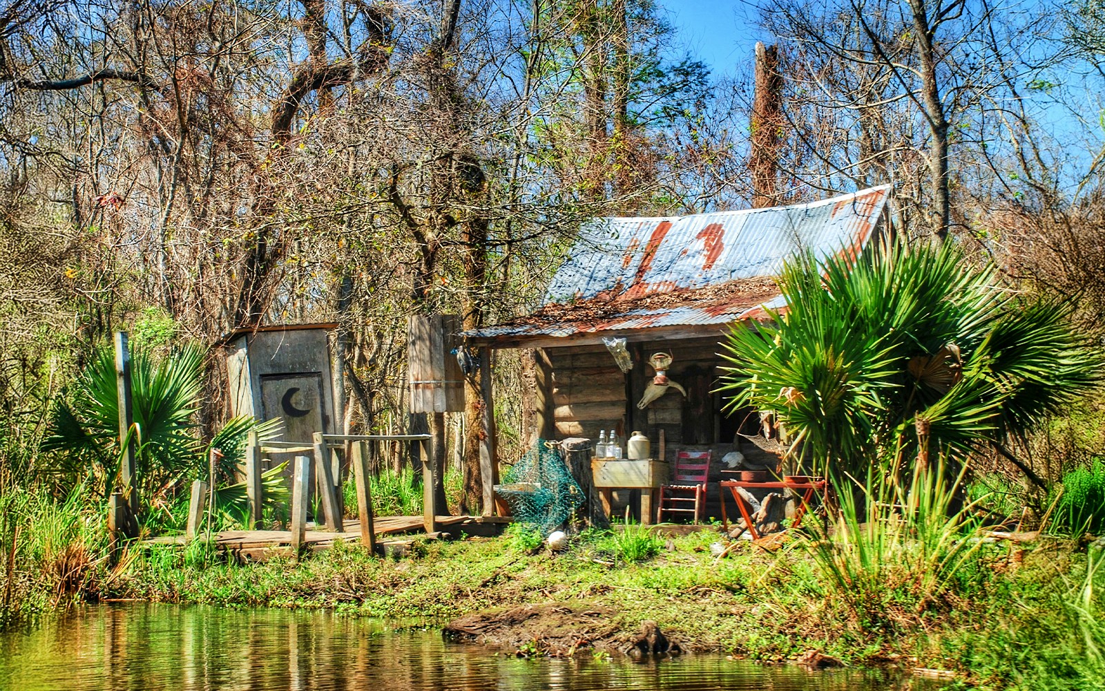 Rustic cabin and outhouse by a swamp, part of the Swamp Tour & Oak Alley Plantation Tour.