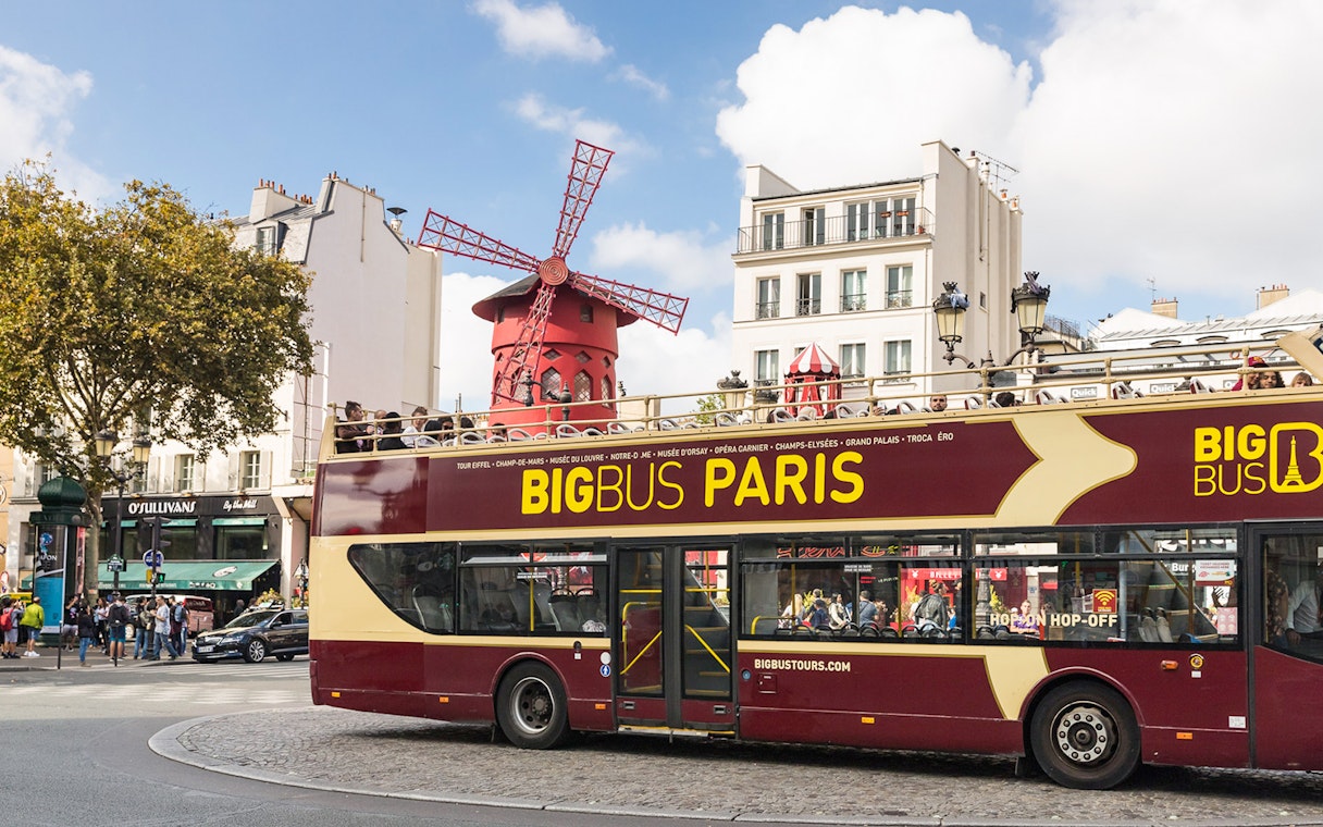 Tourists on BigBus Paris passing Moulin Rouge on hop-on-hop-off tour.