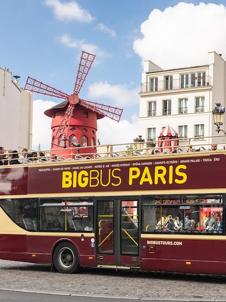 Tourists on BigBus Paris passing Moulin Rouge on hop-on-hop-off tour.