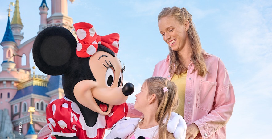 Minnie Mouse greeting a child and adult at Disneyland Paris with Sleeping Beauty Castle in the background.