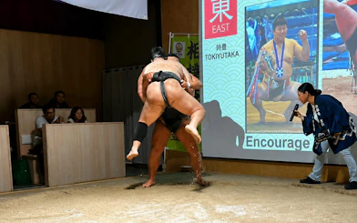 Sumo wrestlers competing in a Kyoto arena with audience watching.
