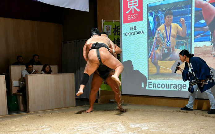 Sumo wrestlers competing in a Kyoto arena with audience watching.