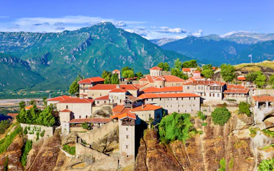 Meteora monasteries perched on cliffs with mountains in the background, Greece.