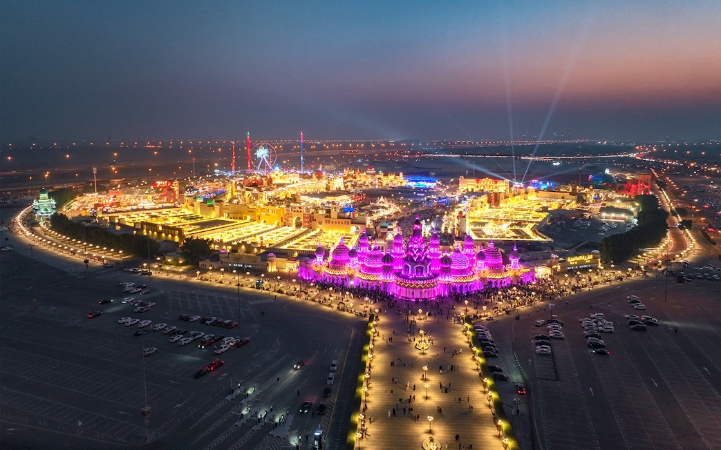 Aerial view of Global Village Dubai at night with vibrant lights and Ferris wheel.