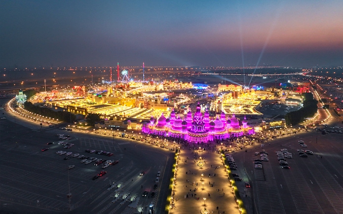 Aerial view of Global Village Dubai at night with vibrant lights and Ferris wheel.