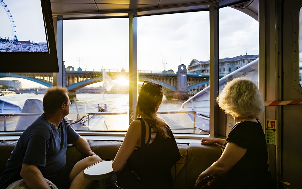 People enjoying a river cruise view of London Bridge at sunset.