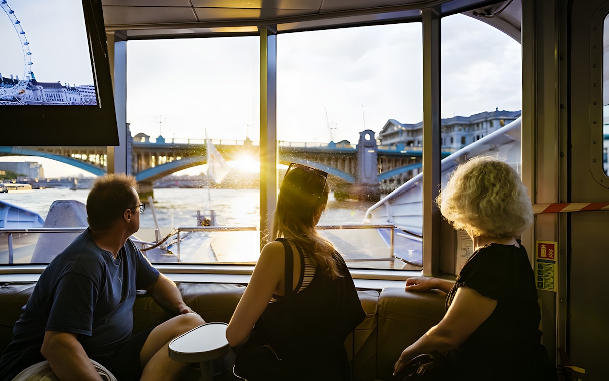 People enjoying a river cruise view of London Bridge at sunset.