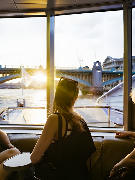 People enjoying a river cruise view of London Bridge at sunset.