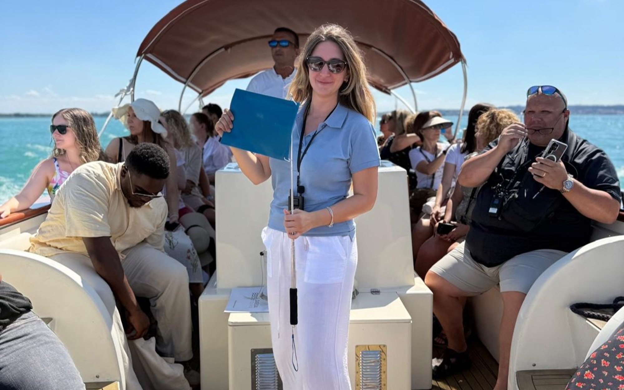 Guide leading a boat tour on Lake Garda with passengers seated.