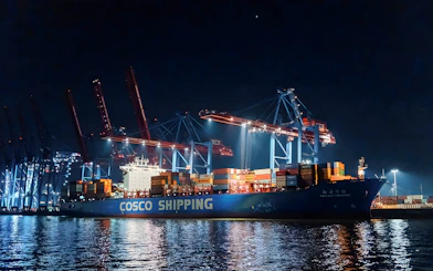 Large ship docked at night with illuminated cranes, part of the 1.5h Grand Evening Lights Cruise.