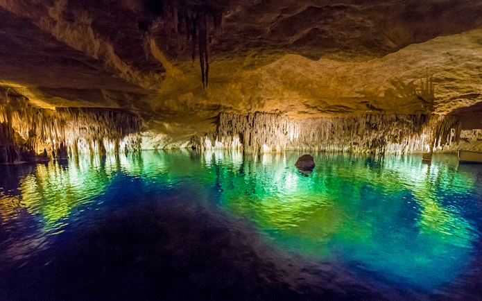 Drach Caves illuminated stalactites reflecting in turquoise water, Mallorca.