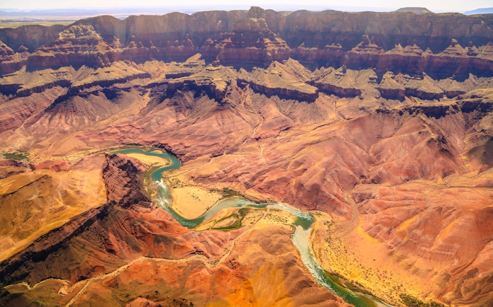 Aerial view of the Grand Canyon with winding Colorado River and layered rock formations.