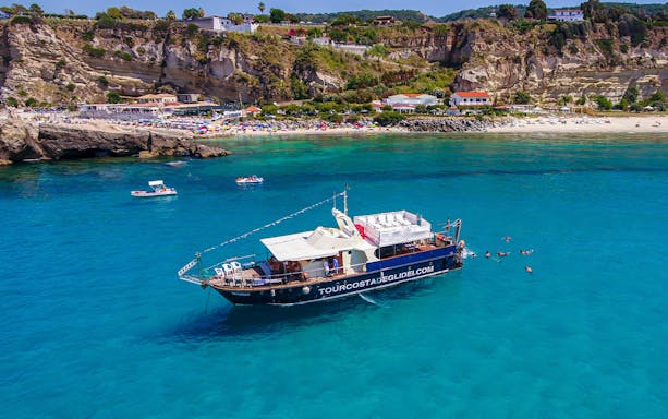 Boat on clear waters near Tropea beach, Italy, with swimmers nearby.
