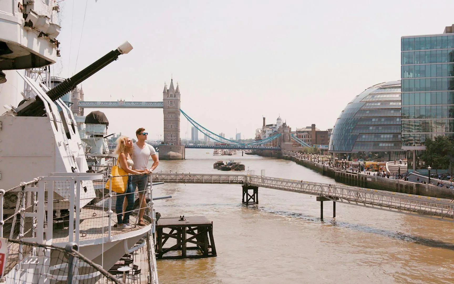Couple on HMS Belfast with Tower Bridge and City Hall in London background.