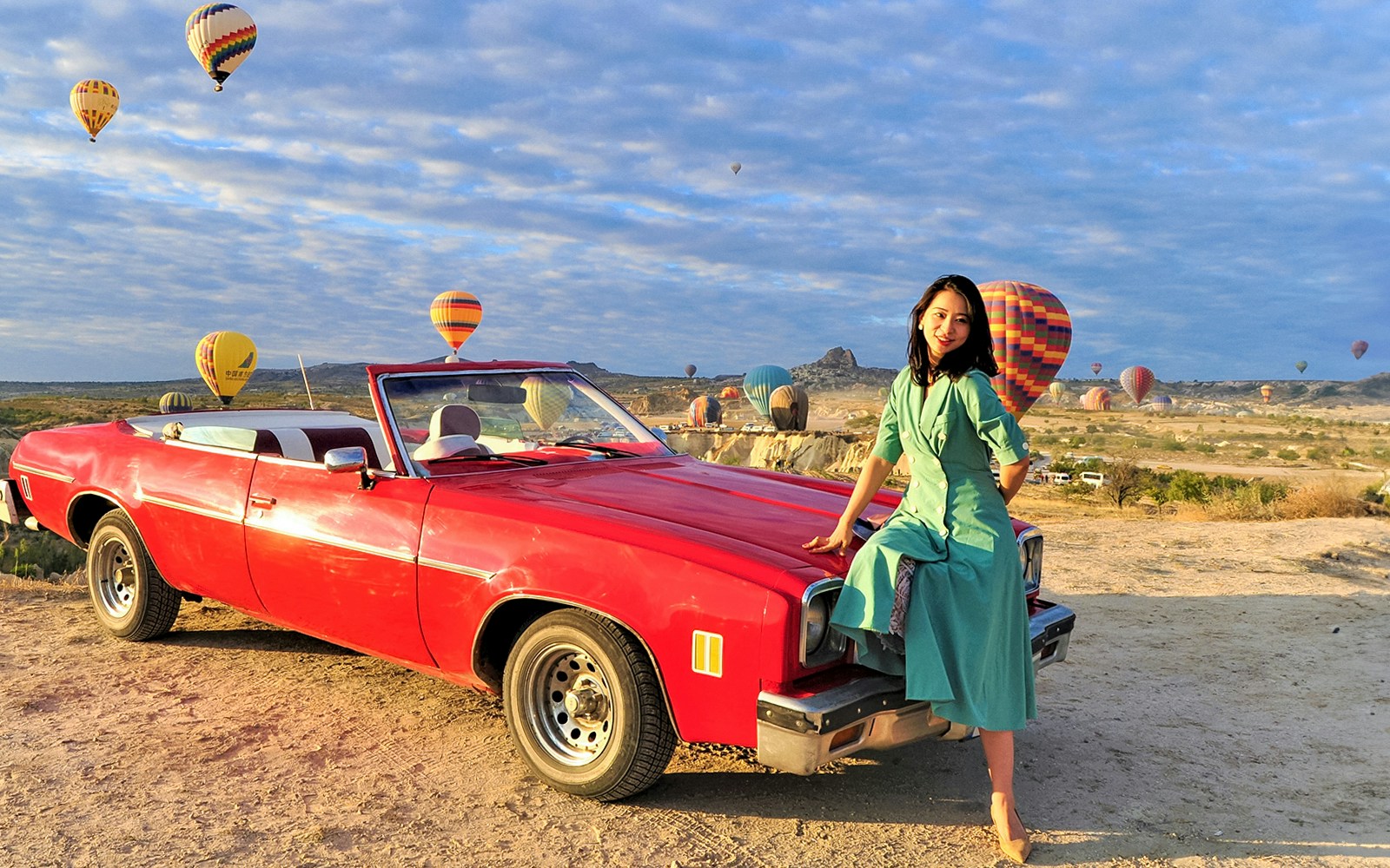 Vintage car with a person in front of hot air balloons in Göreme, Cappadocia.