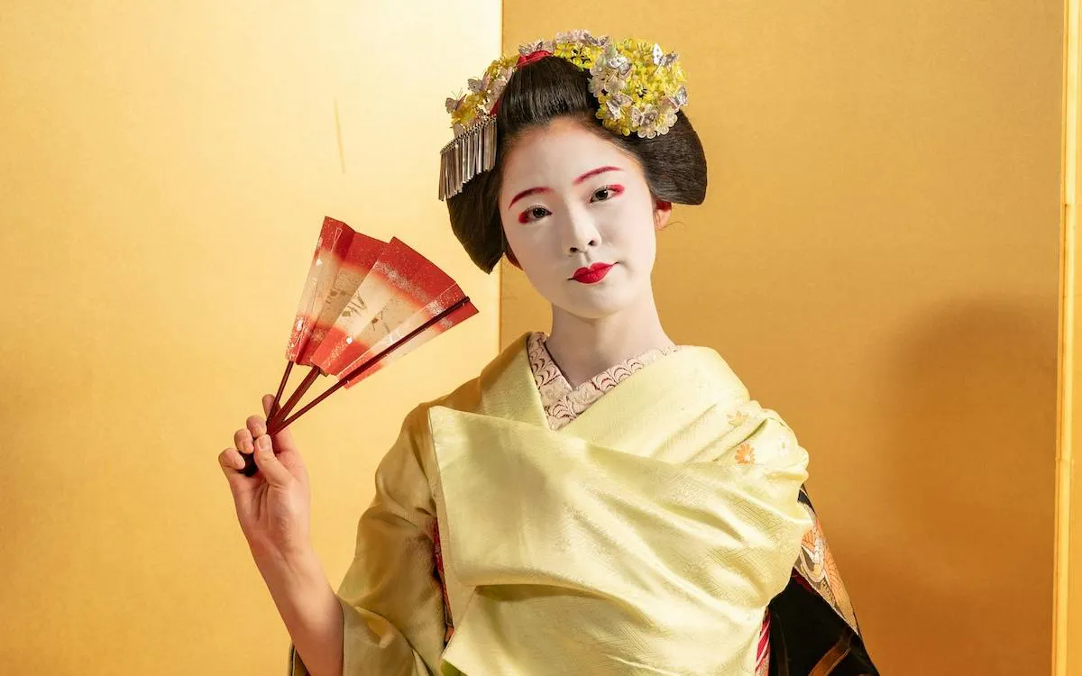 Maiko in traditional attire holding a fan during Kyoto Kaiseki dinner tour.