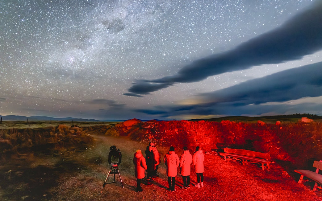 Tourists stargazing at The Crater under a starry sky with telescope.