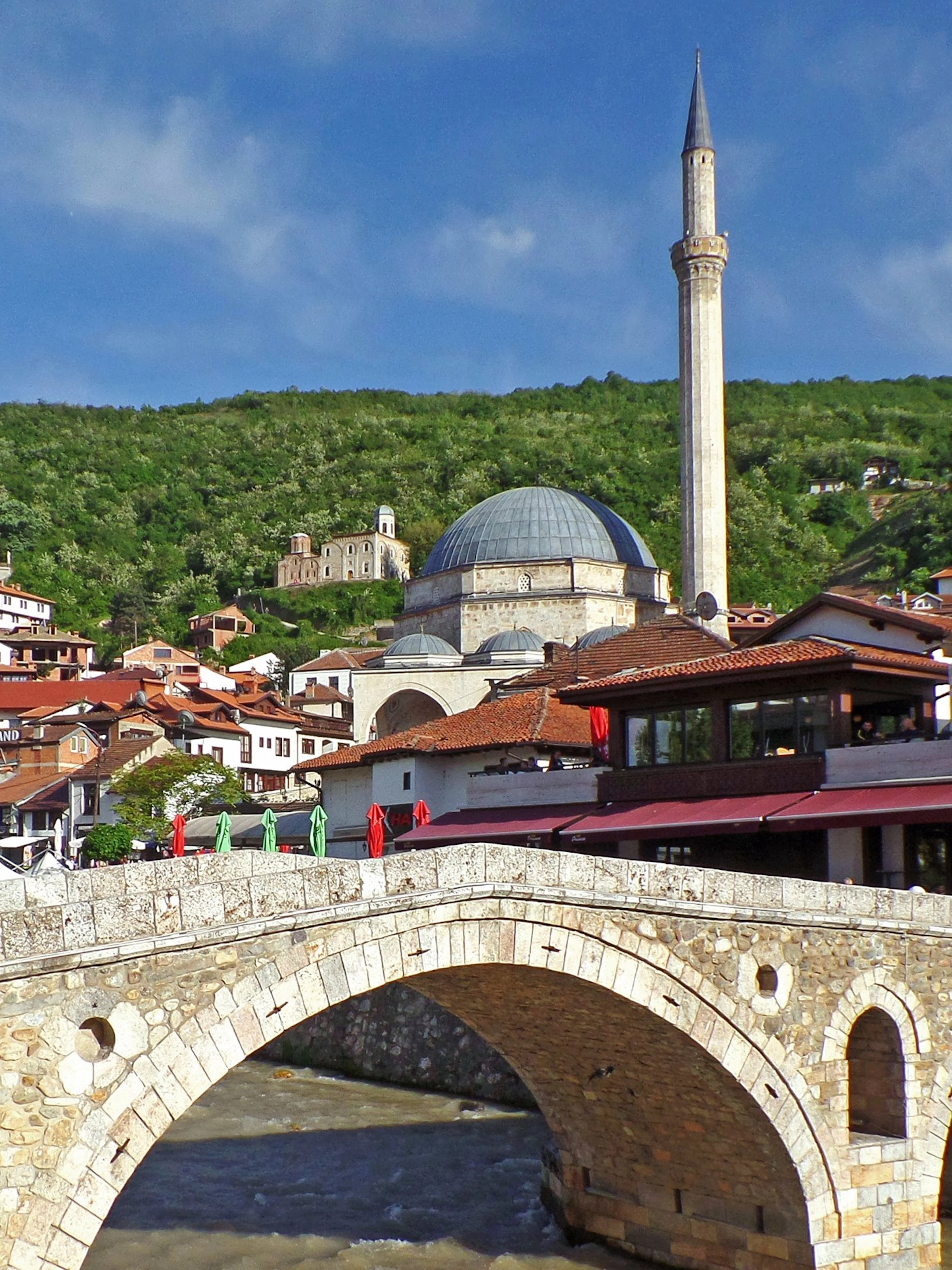 Old stone bridge over river with mosque and hillside houses in Prizren Old City, Kosovo.