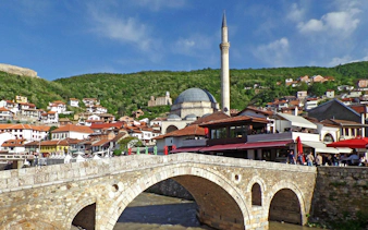 Old stone bridge over river with mosque and hillside houses in Prizren Old City, Kosovo.