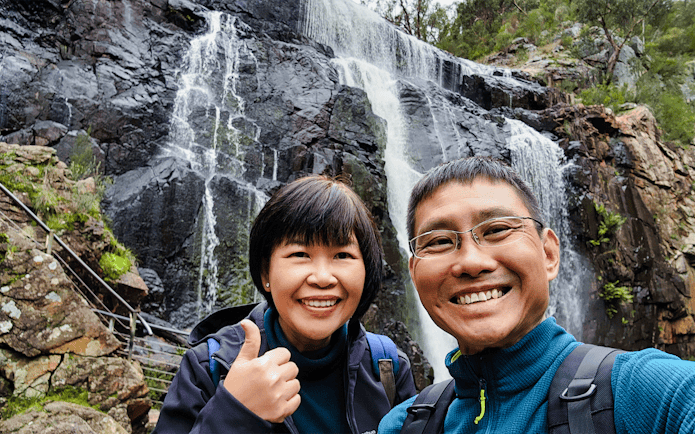 Visitors smiling in front of MacKenzie Falls, Grampians National Park.