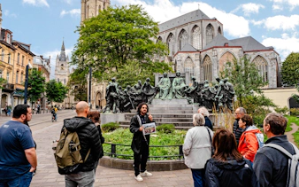 Tour group listening to a guide near a historic monument in Ghent city center, Belgium.