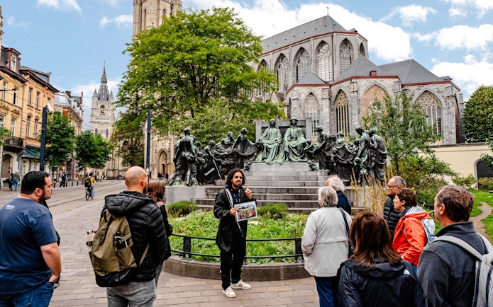 Tour group listening to a guide near a historic monument in Ghent city center, Belgium.