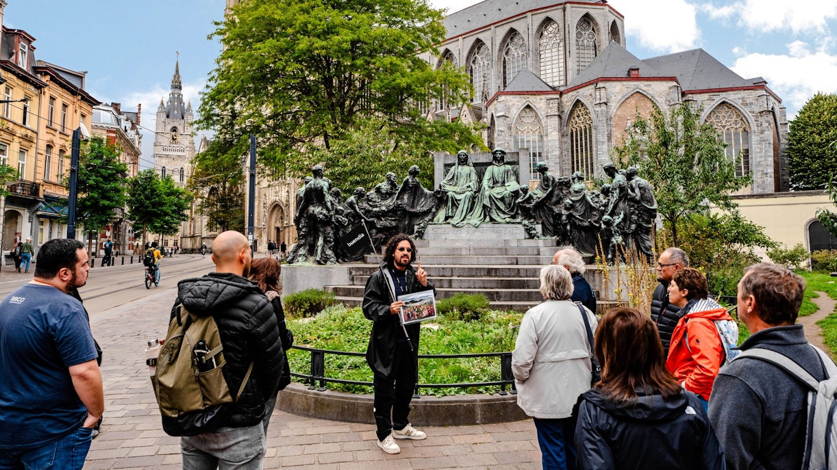 Tour group listening to a guide near a historic monument in Ghent city center, Belgium.