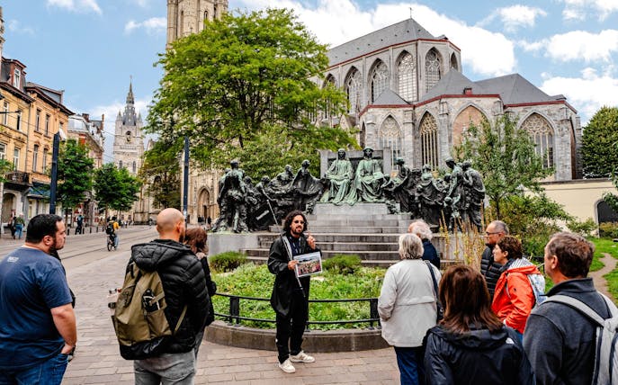 Tour group listening to a guide near a historic monument in Ghent city center, Belgium.