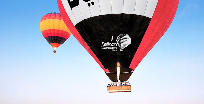 Hot air balloons over Dubai desert with "Dubai" text on balloon.