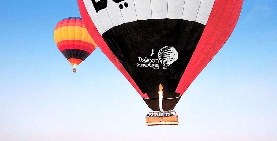 Hot air balloons over Dubai desert with "Dubai" text on balloon.