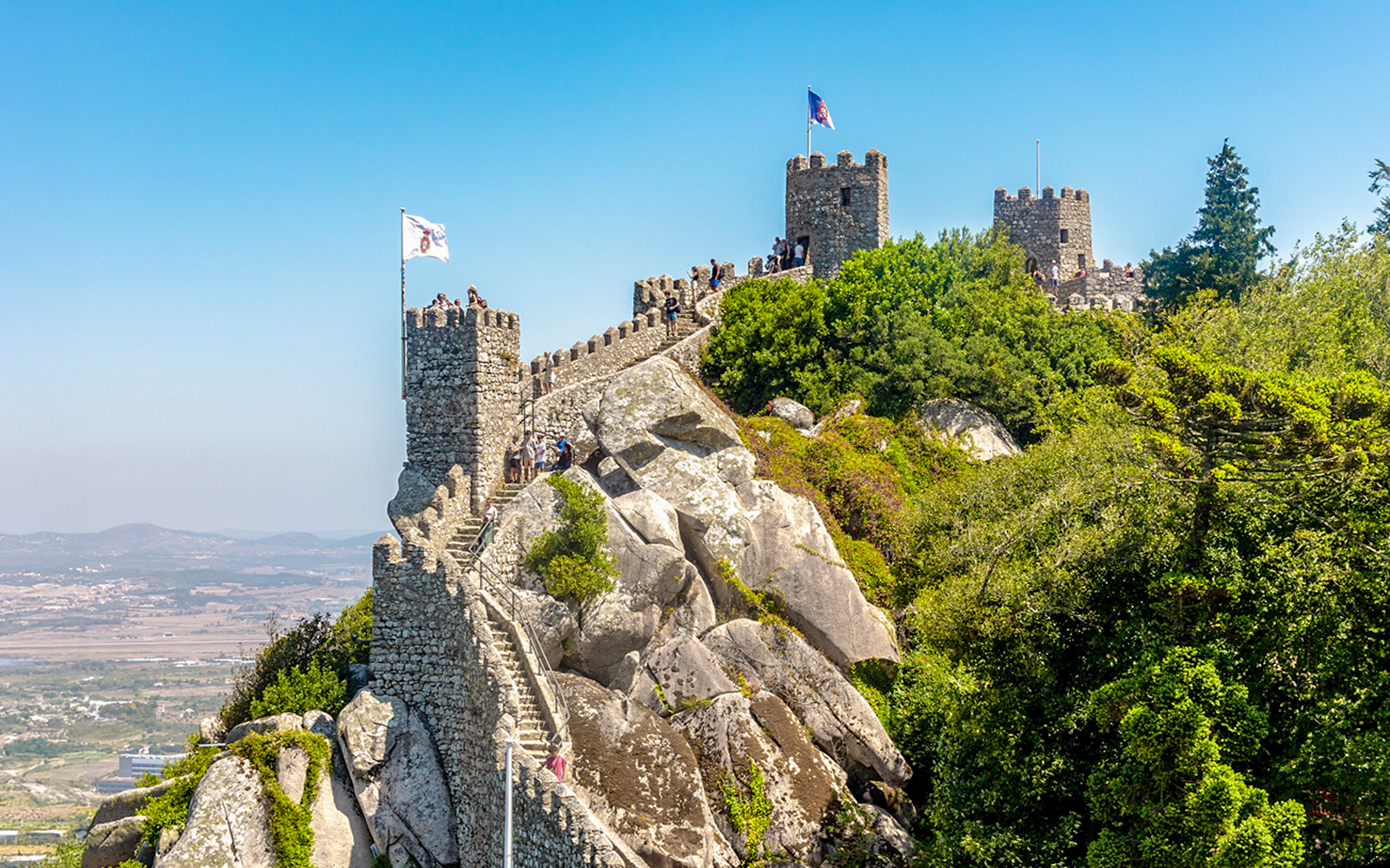 Moorish Castle on hilltop with visitors, overlooking Sintra's lush landscape, Portugal.