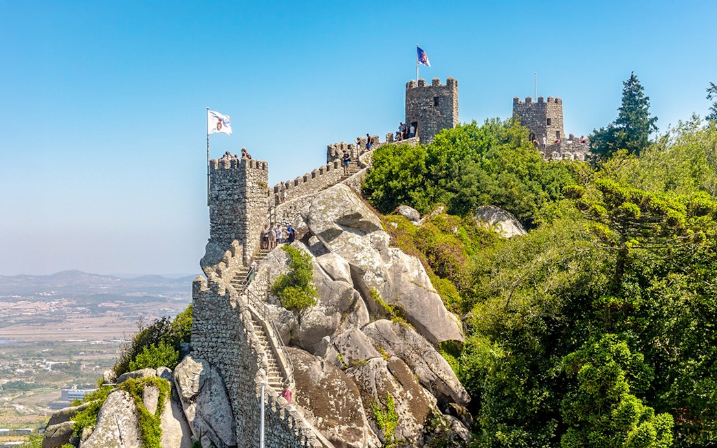 Moorish Castle on hilltop with visitors, overlooking Sintra's lush landscape, Portugal.