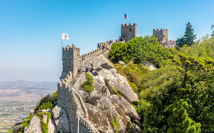 Moorish Castle on hilltop with visitors, overlooking Sintra's lush landscape, Portugal.