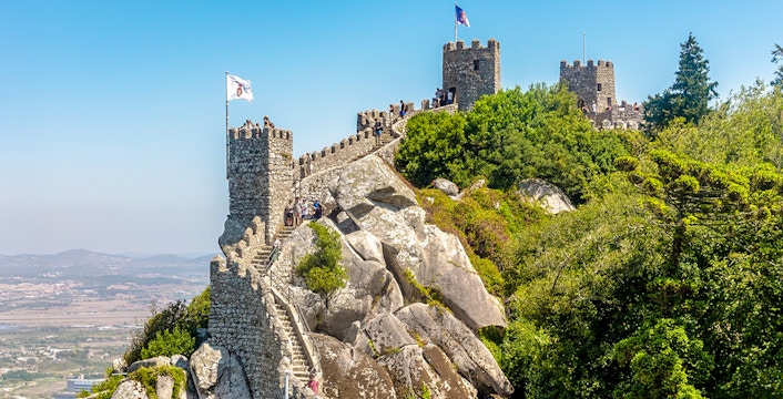 Moorish Castle on hilltop with visitors, overlooking Sintra's lush landscape, Portugal.