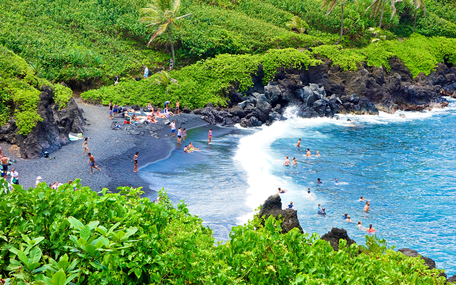 Aerial view of black sand beach with swimmers at Waianapanapa State Park, Maui, Hawaii.