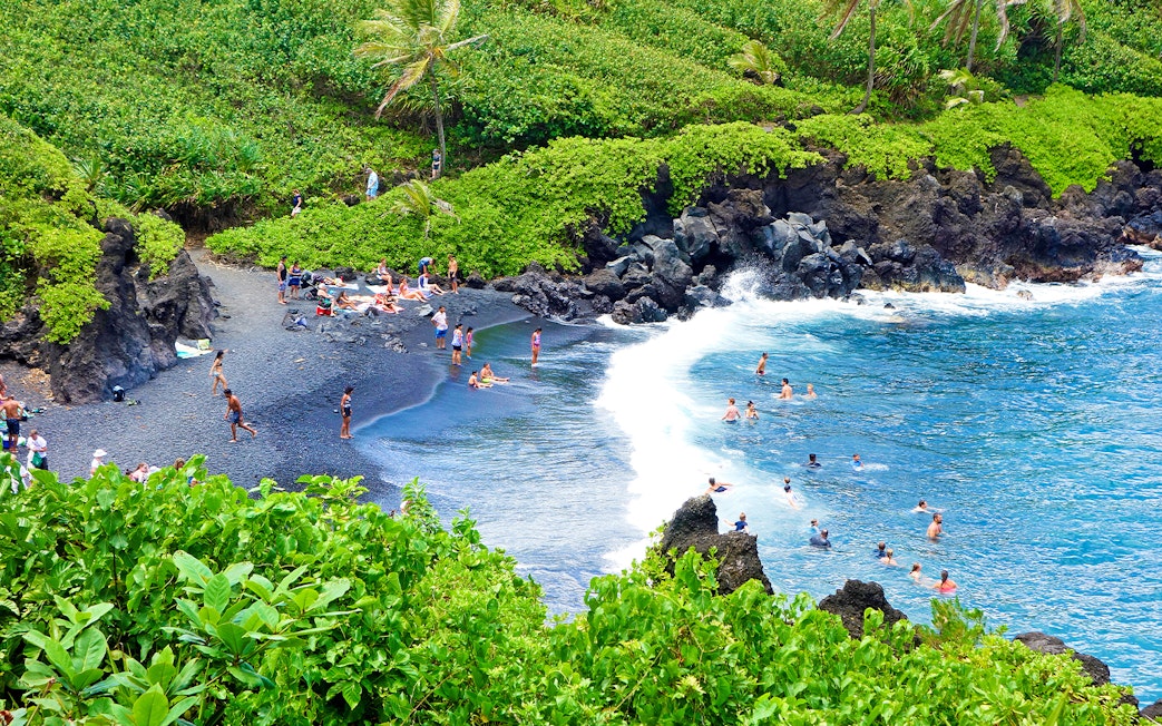Aerial view of black sand beach with swimmers at Waianapanapa State Park, Maui, Hawaii.