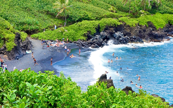 Aerial view of black sand beach with swimmers at Waianapanapa State Park, Maui, Hawaii.