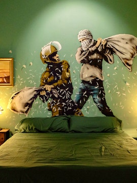 Wall art of two figures pillow fighting above a bed at The Banksy Museum.
