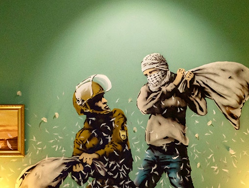 Wall art of two figures pillow fighting above a bed at The Banksy Museum.