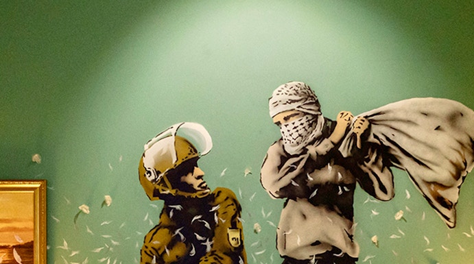 Wall art of two figures pillow fighting above a bed at The Banksy Museum.