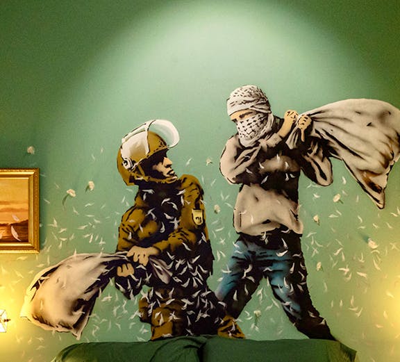 Wall art of two figures pillow fighting above a bed at The Banksy Museum.