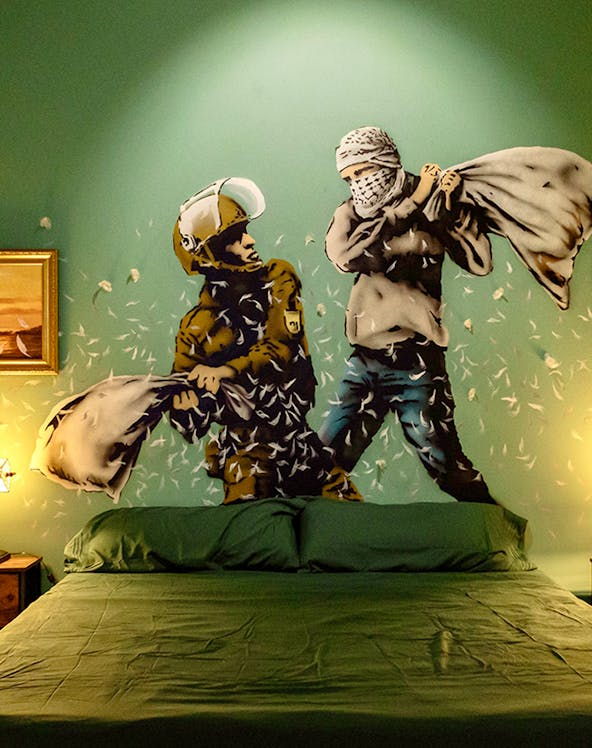 Wall art of two figures pillow fighting above a bed at The Banksy Museum.