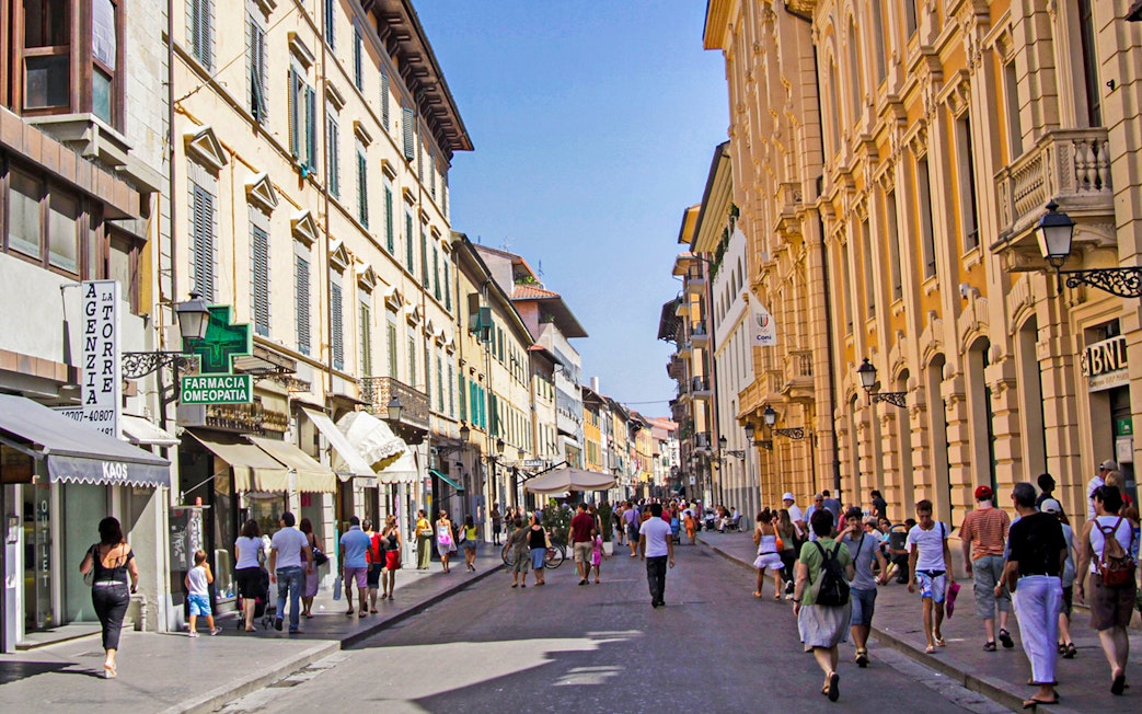People walking along a bustling street in Pisa, Italy, lined with historic buildings.