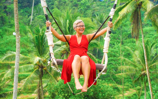 Woman on swing at Alas Harum Bali with lush greenery in background.