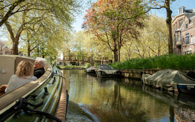 Couple enjoying a canal cruise in Utrecht with scenic views of trees and historic buildings.